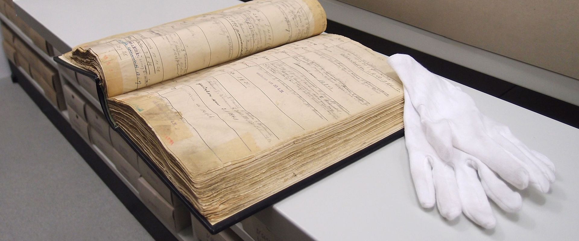 Open historical book from the Freudenberg archives next to a pair of white gloves.