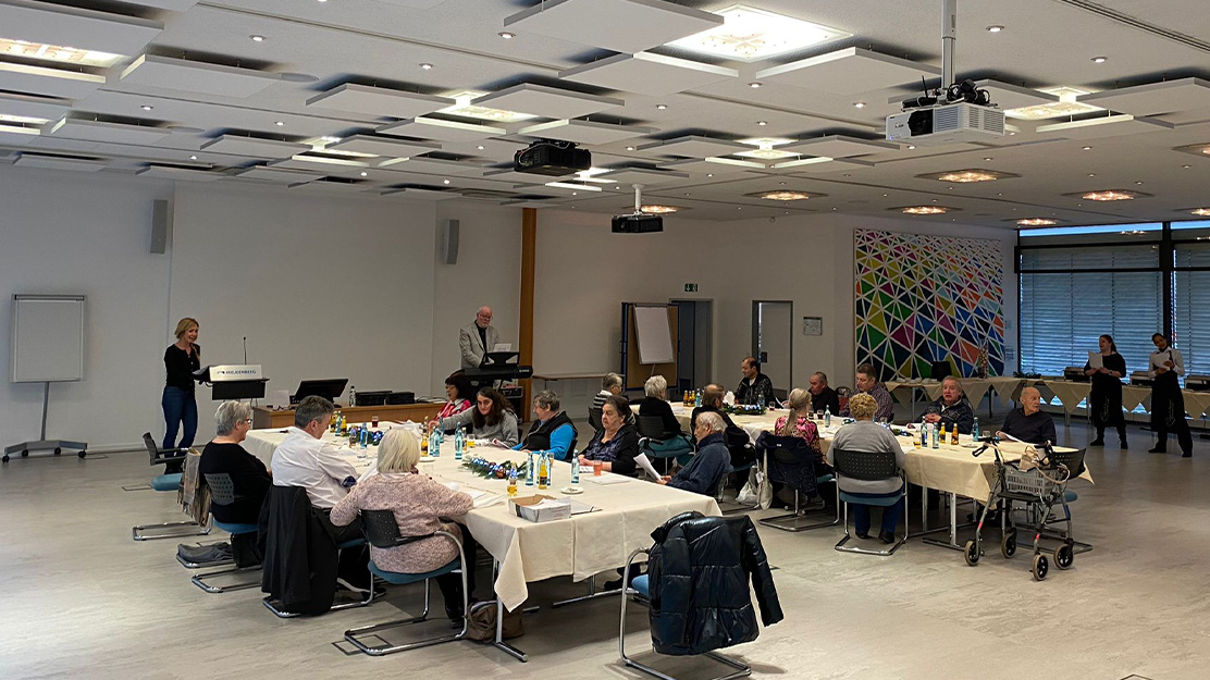 Foto zeigt einen Raum mit zwei großen Tischen, an welchen Menschen im hohen Alter sitzen