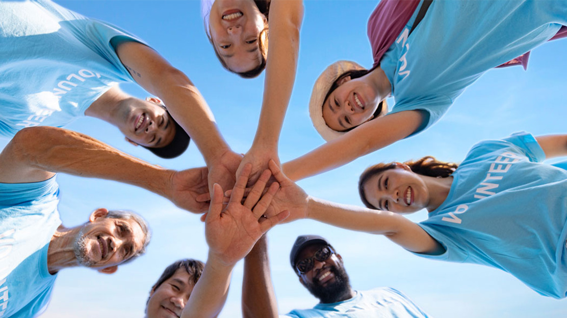 Foto zeigt eine Gruppe von Menschen, die im Kreis stehen und ihre Hände aufeinander legen