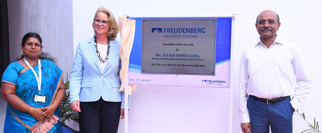 Three people in front of a sign that was hung up to mark the laying of the foundation stone