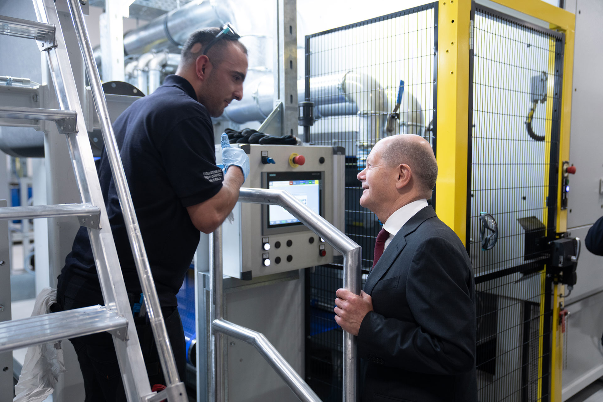 Picture shows two men standing in a production plant and talking to each other