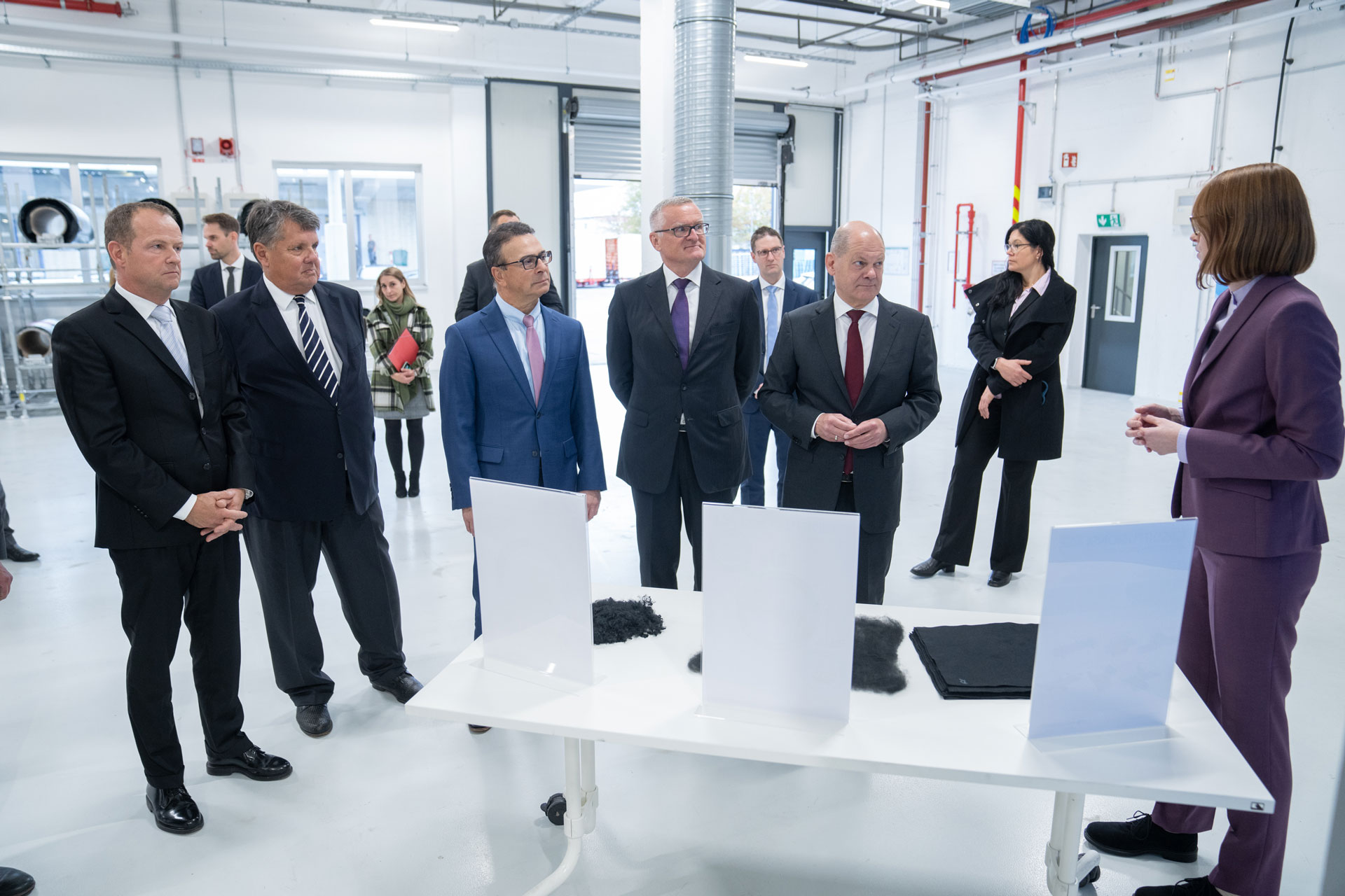 Five men in the foreground stand next to each other and look at a woman on the right side of the picture who is talking to them