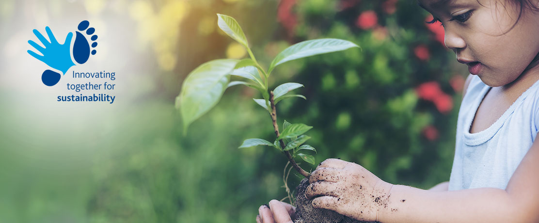 Pictures shows a child with muddy hands holding a little plant and looking at it
