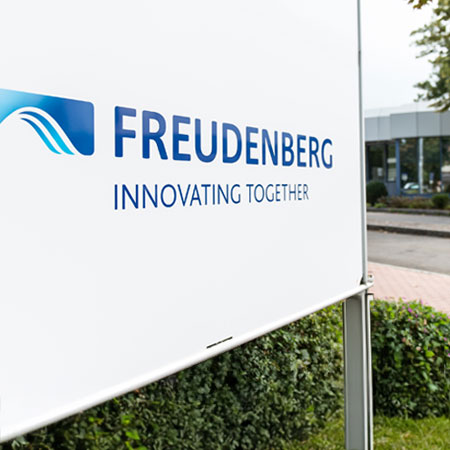 Erfahren Sie mehr über Freudenberg Weißes Schild mit der Aufschrift Freudenberg Innovation Together in blauen Buchstaben