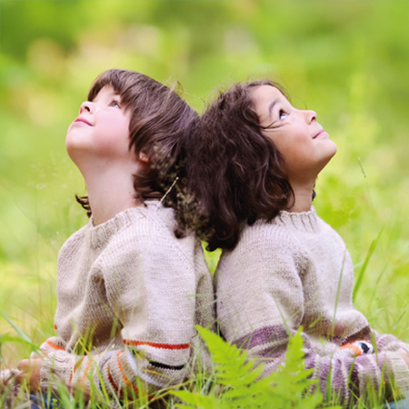 Learn more about Freudenberg's activities in Social Responsibility Picture shows two young children sitting back to back in the gras watching the sky.