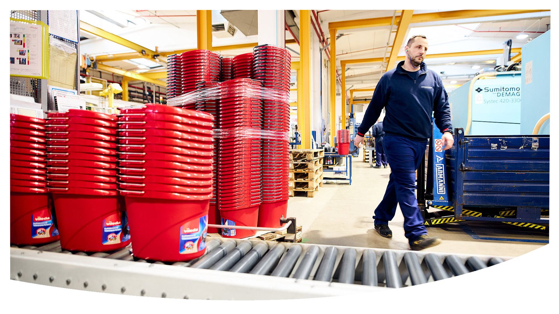 A man in a manufacturing hall walking next to hundreds of red Vileda buckets