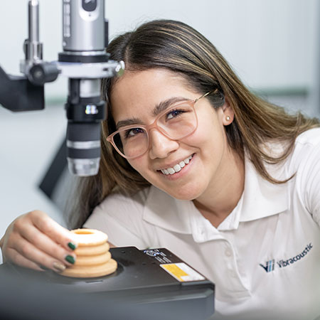 A woman sitting in front of a microscope is looking into the camera