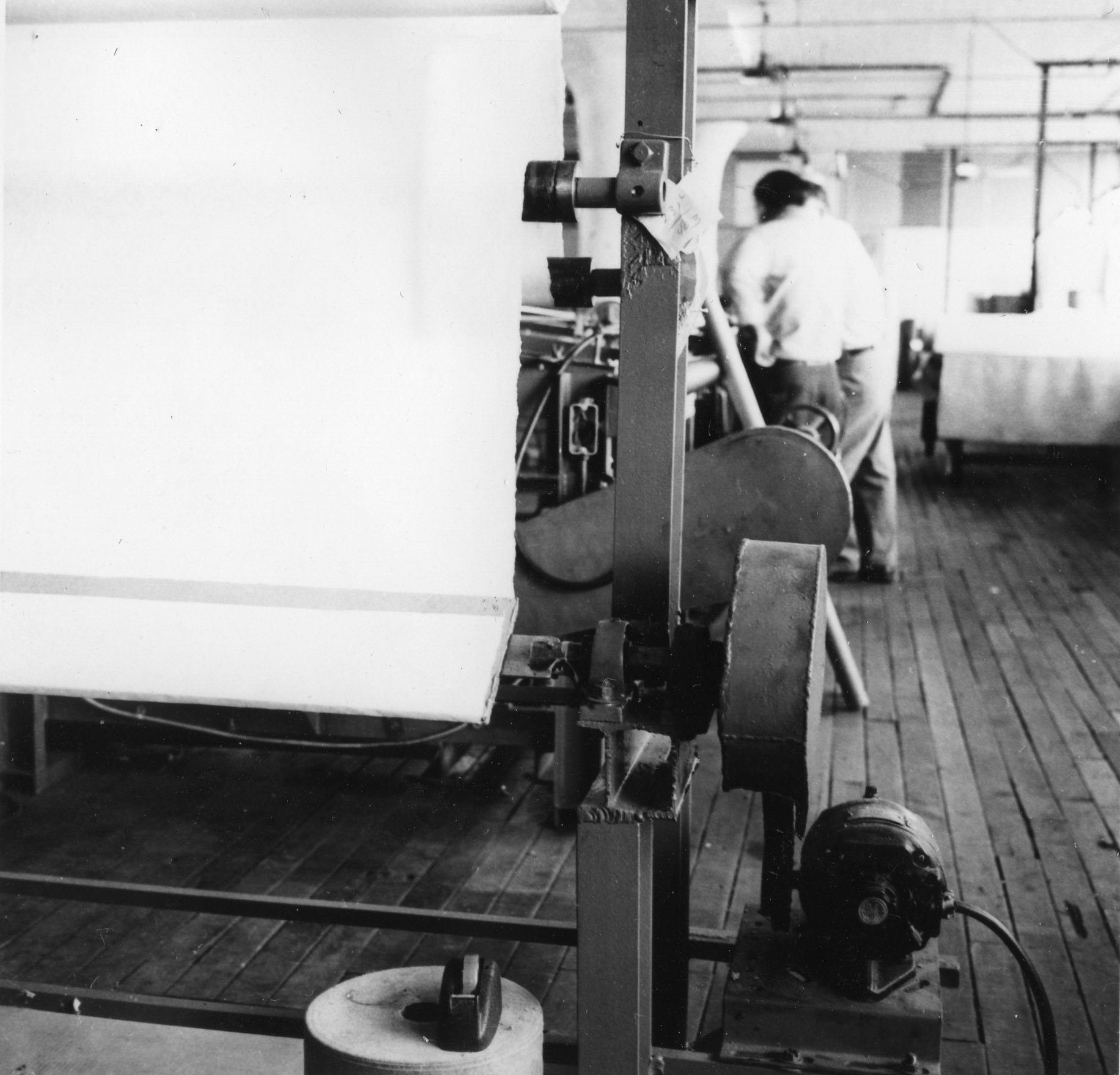 Picture shows an old looking, grey photo of a room with a machine for nonwoven production