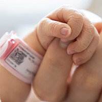 Eine winzige Babyhand, die den Finger einer Erwachsenenhand umgreift.