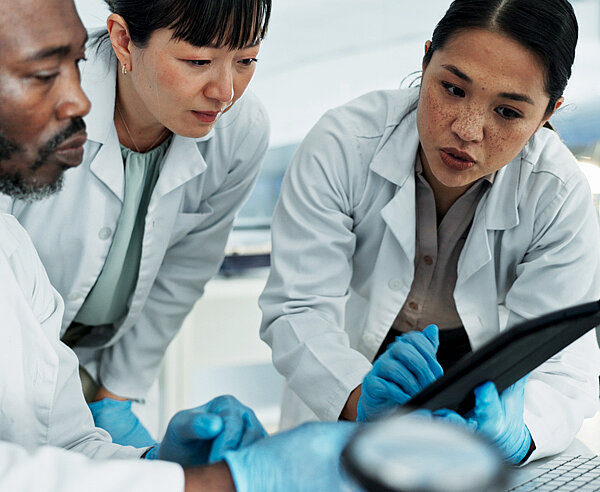 Drei Mitarbeiter schauen in einem Labor auf ein Tablet.