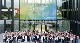 A large group of people raising their hands in the air and smiling into the camera