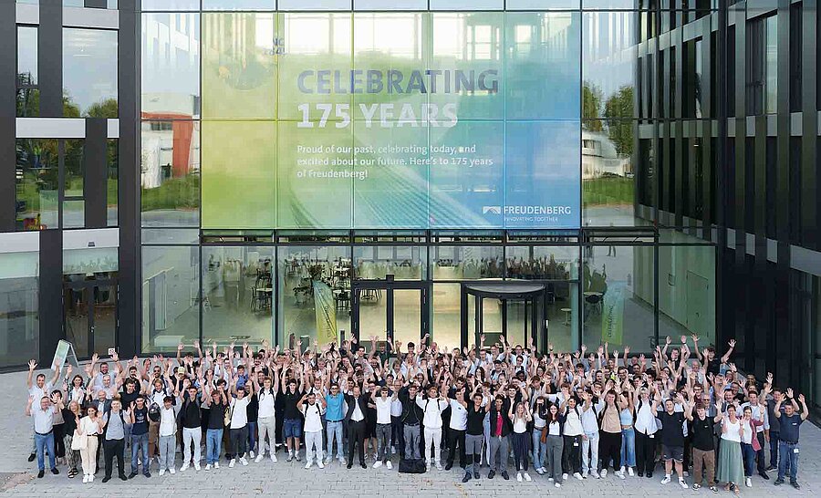 A large group of people raising their hands in the air and smiling into the camera