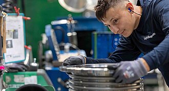 The picture shows a man in a workshop working on a round object