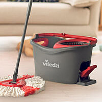 Ein Vileda-Mopp und ein grauer Vileda-Eimer vor einem Sofa