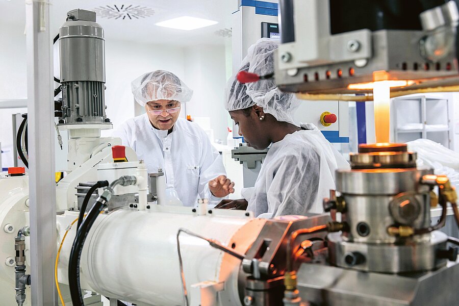 A man and a woman wearing white coats and hairnets stand behind a piece of laboratory equipment, working intently.