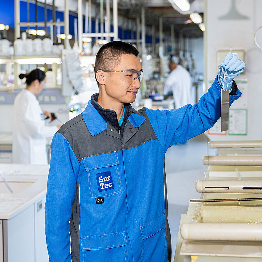 Person in blue workwear wearing protective gloves holds a sample strip in an industrial production environment