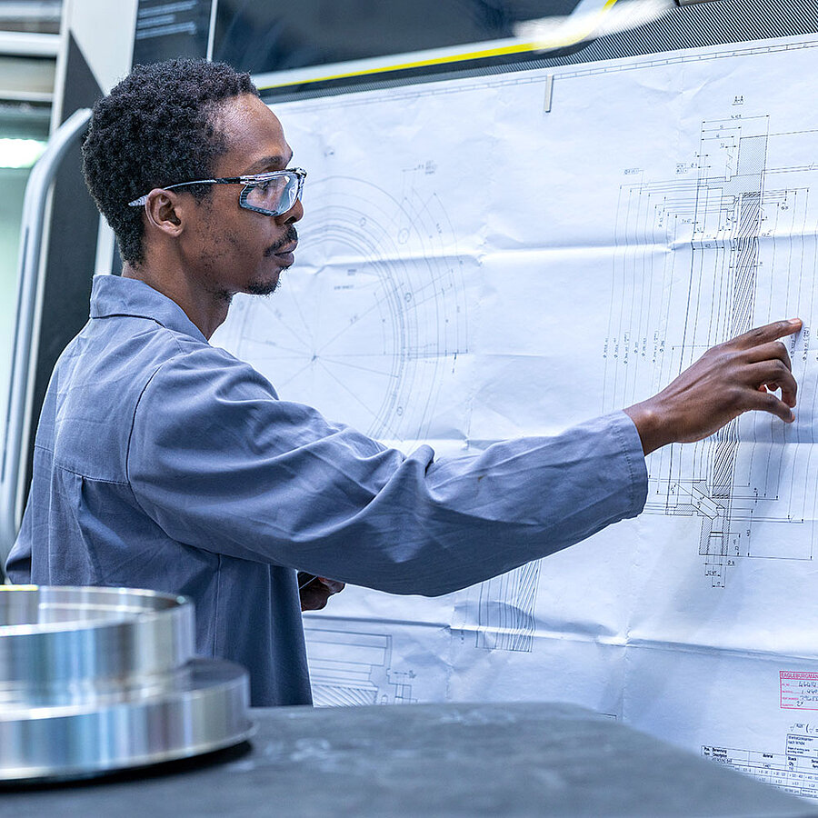 Person in workwear points to a large technical drawing