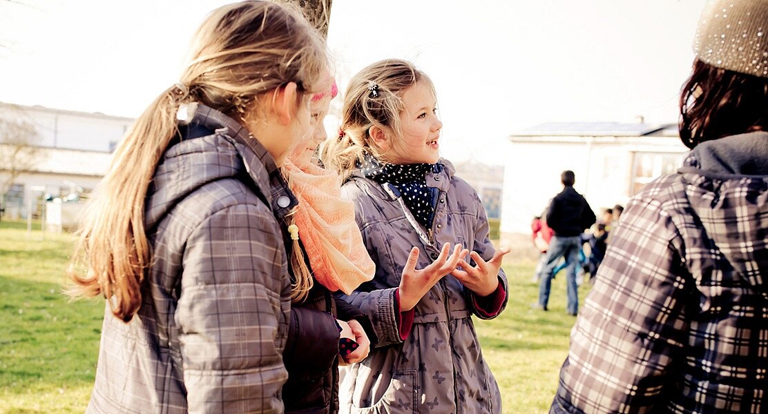 Drei Kinder, die nebeneinander stehen und miteinander sprechen