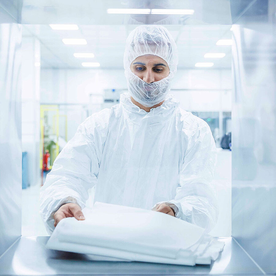 Worker wearing protective clothing holding folded nonwoven fabric in a cleanroom environment.