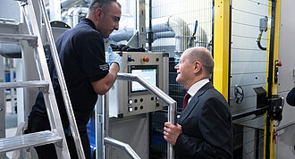 Picture shows two men standing in a production plant and talking to each other